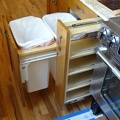 The trash bins and spice rack next to oven
